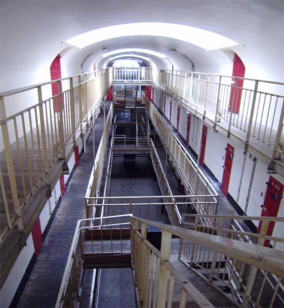 A high-angle view looking down the multi-tiered corridor of a historic prison block.