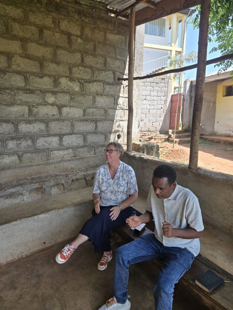 Marie-Louise Norozi and a colleague seated on a concrete bench under a shelter at the prison