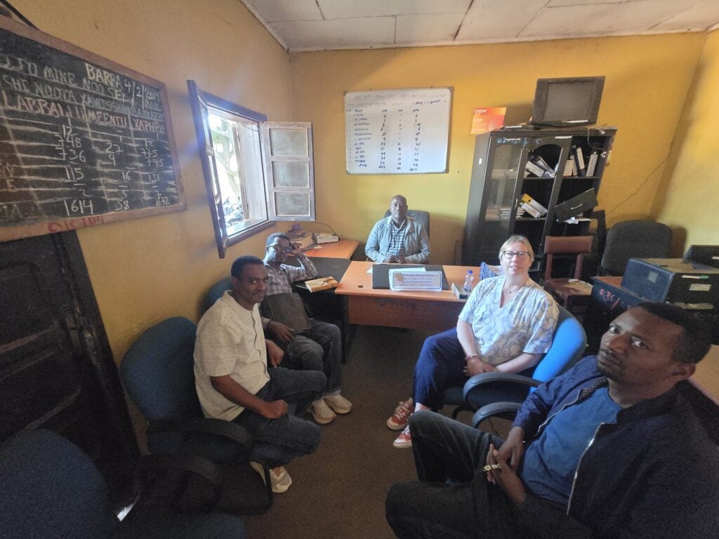 Marie-Louise Norozi and colleagues seated in the commissioner's office, with a chalkboard and a whiteboard on the walls